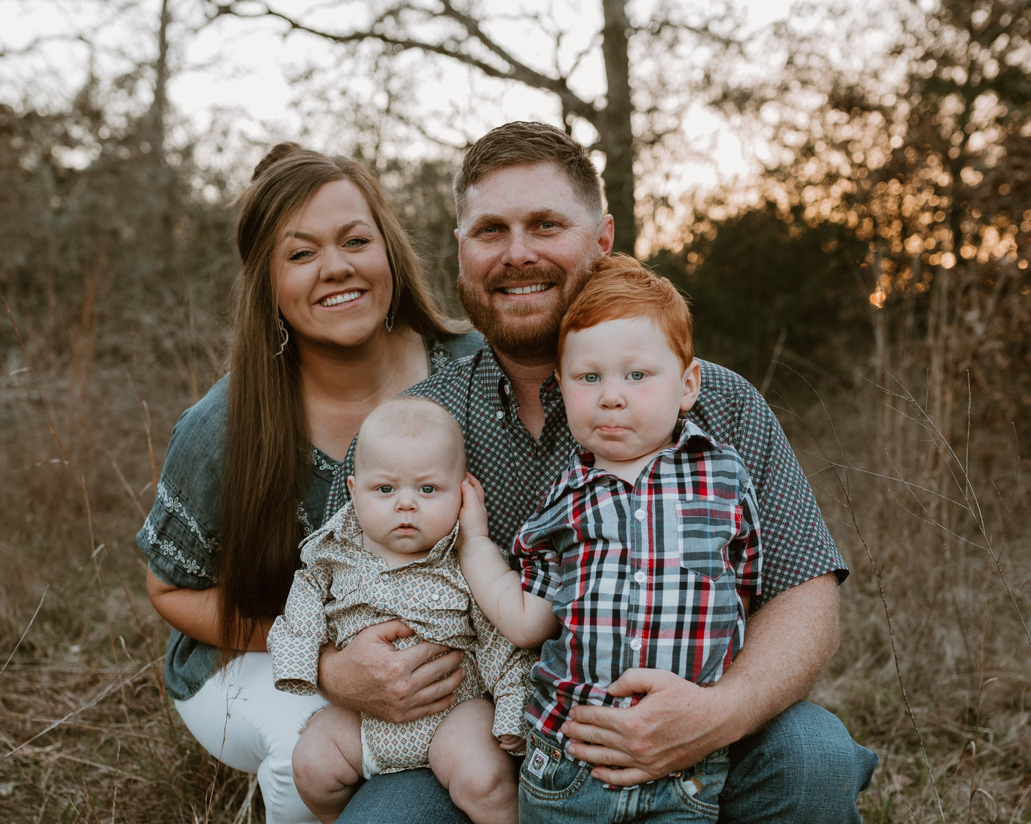Family of four outdoors in a natural setting with trees and grass.